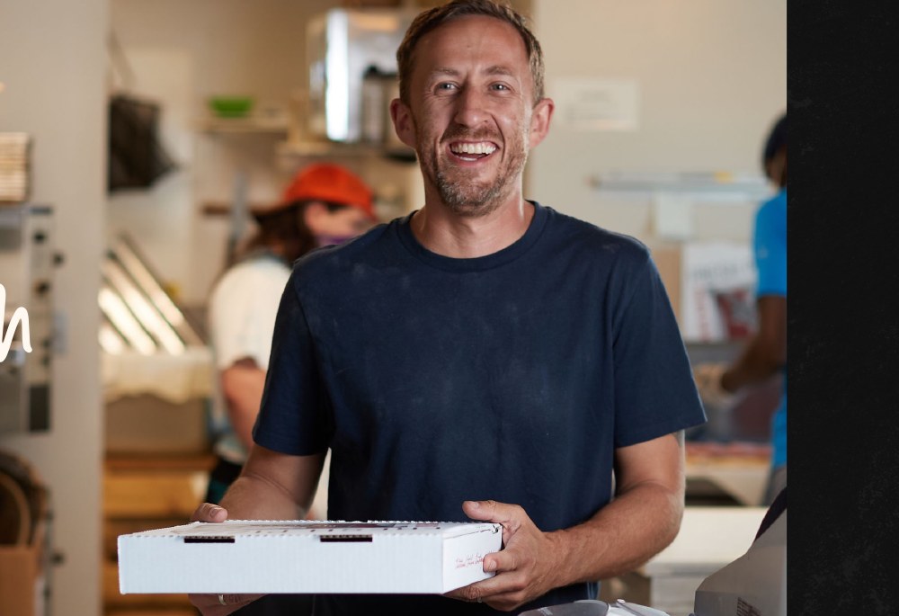 Lena's owner Matt Swank holding a fresh pizza box in the kitchen
